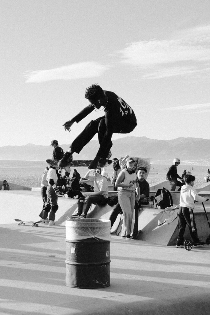 Dramatic black and white shot of a skateboarder mid-air at a busy skatepark.