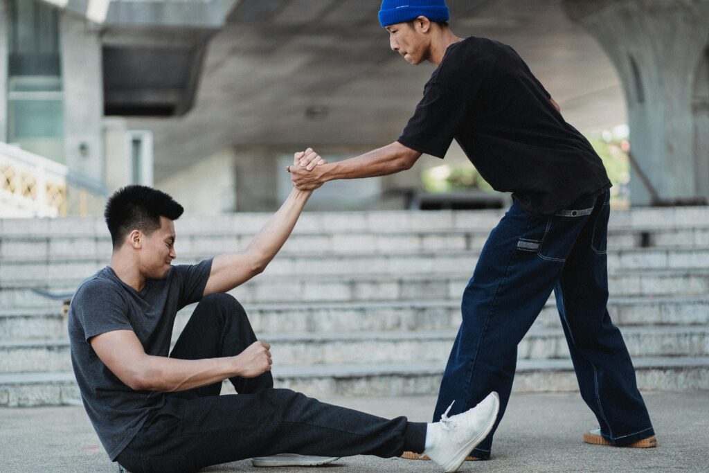 Two young men helping each other on urban city stairs, symbolizing friendship and support.