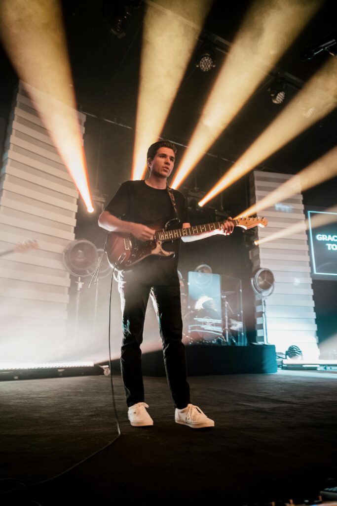 A guitarist passionately playing electric guitar under bright stage lights during a live concert.